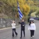 Τρία άτομο περπατούν σε δρόμο κρατώντας ελληνική σημαία