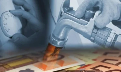 Χέρι να ρυθμίζει θερμοστάτη, ακροφύσιο αντλίας και χαρτονομίσματα ευρώ στο κάτω μέρος.