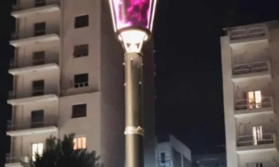 Φωτιστικός στύλος με μουτζουρωμένο φως τη νύχτα και πολυκατοικίες στο βάθος.