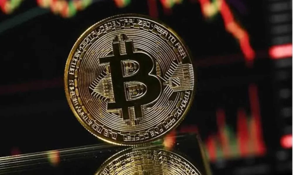 Χρυσά κέρματα Bitcoin μπροστά από οθόνη με κόκκινα και πράσινα διαγράμματα αγοράς