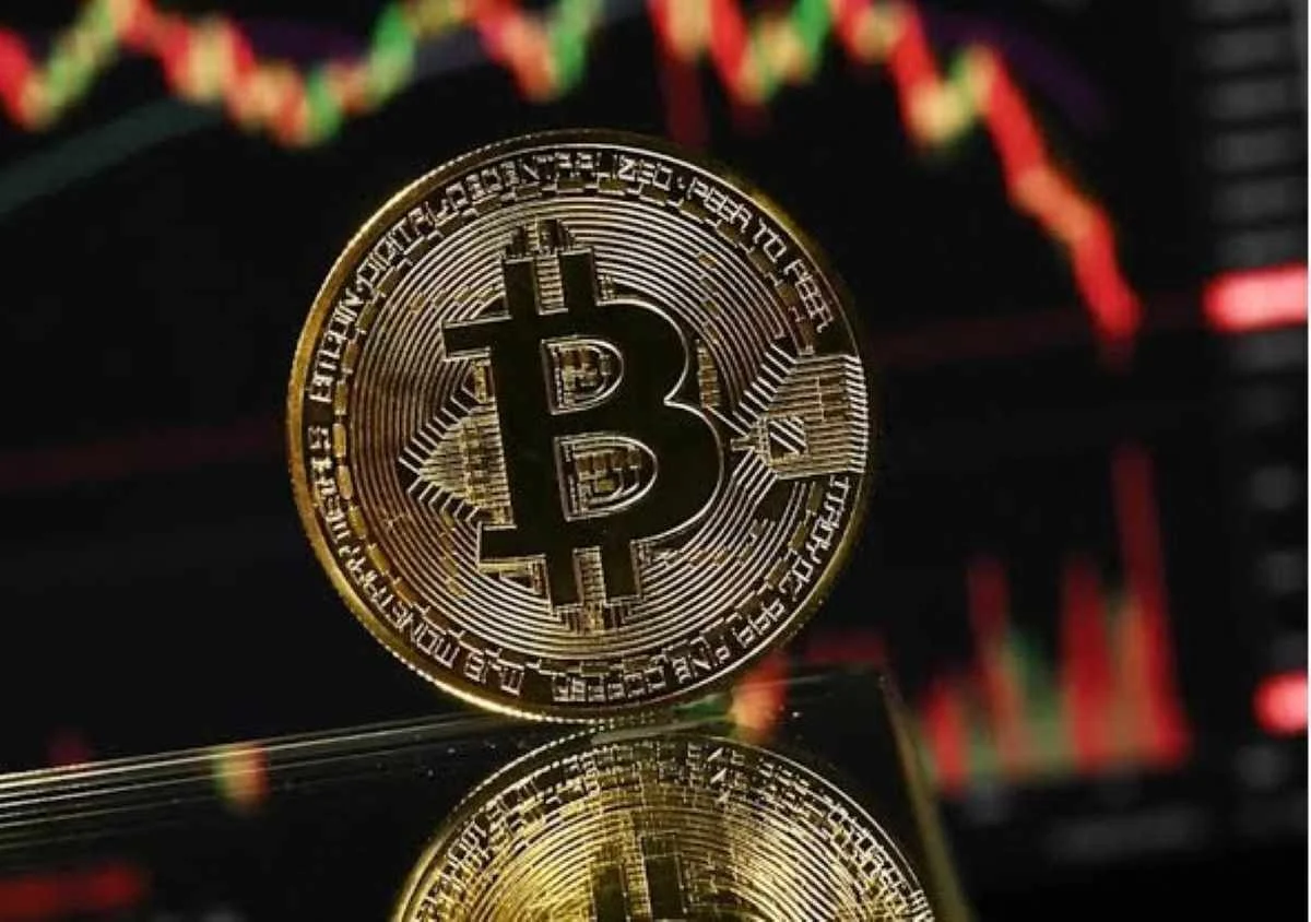Χρυσά κέρματα Bitcoin μπροστά από οθόνη με κόκκινα και πράσινα διαγράμματα αγοράς