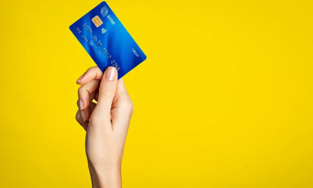 Χέρι κρατάει μπλε πιστωτική κάρτα σε κίτρινο φόντο.