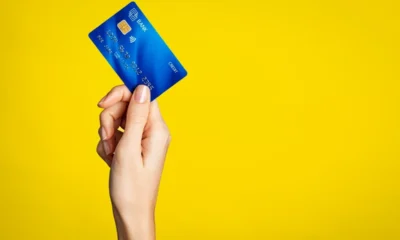 Χέρι κρατάει μπλε πιστωτική κάρτα σε κίτρινο φόντο.