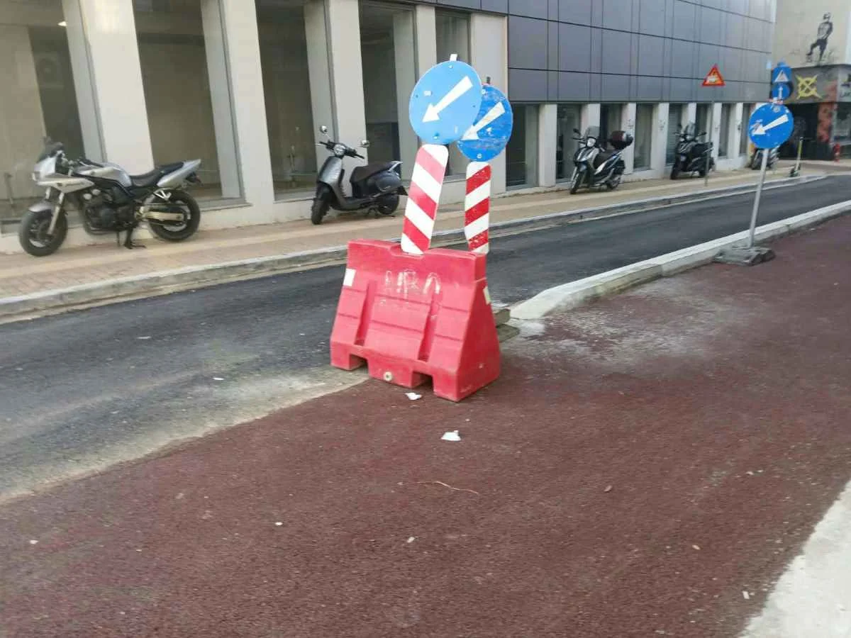 Δρόμος με κόκκινο διάδρομο, πορτοκαλί πλαστικό εμπόδιο και μπλε πινακίδες σήμανσης.